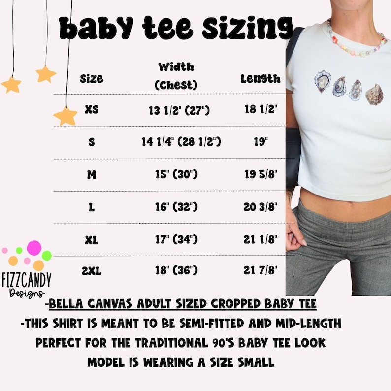 Puede incluir: Una tabla de tallas para una camiseta de beb&eacute; recortada, que muestra las medidas de ancho y largo en pulgadas para las tallas XS a 2XL. La tabla est&aacute; sobre un fondo rosa con estrellas blancas y texto. La modelo lleva una talla peque&ntilde;a.