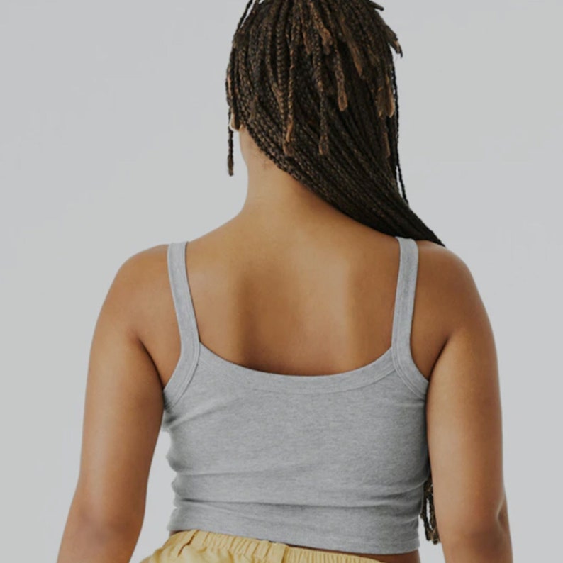 May include: A woman wearing a gray tank top with thin straps. The tank top has a scoop neck and a relaxed fit.