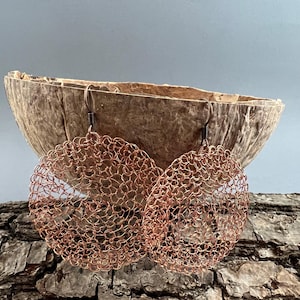 以下が含まれることがあります： 大きな丸い銅線製のイヤリングのペア。イヤリングは繊細な透かし彫りのデザインで、温かみのある金属の仕上げになっています。