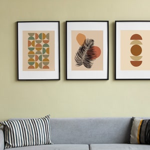 May include: Three framed abstract art prints with geometric shapes and a palm leaf design in shades of brown, orange, green, and beige.