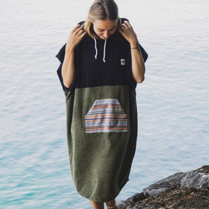 Può includere: Un poncho con cappuccio nero e verde oliva, con una tasca anteriore con un motivo a righe. La persona indossa il poncho vicino all'acqua.