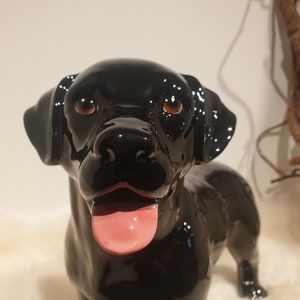 Könnte beinhalten: Schwarze Keramik-Hundefigur mit glänzender Oberfläche. Der Hund hat braune Augen und eine rosa Zunge, die herausstreckt.