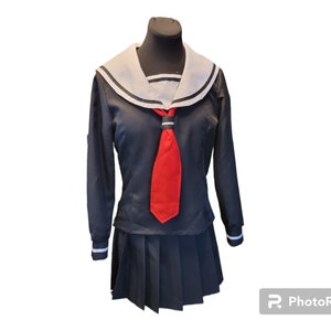 Pode incluir: Um uniforme de marinheiro com colar branco e preto e gravata vermelha. O uniforme inclui uma camisa de manga comprida e uma saia plissada.