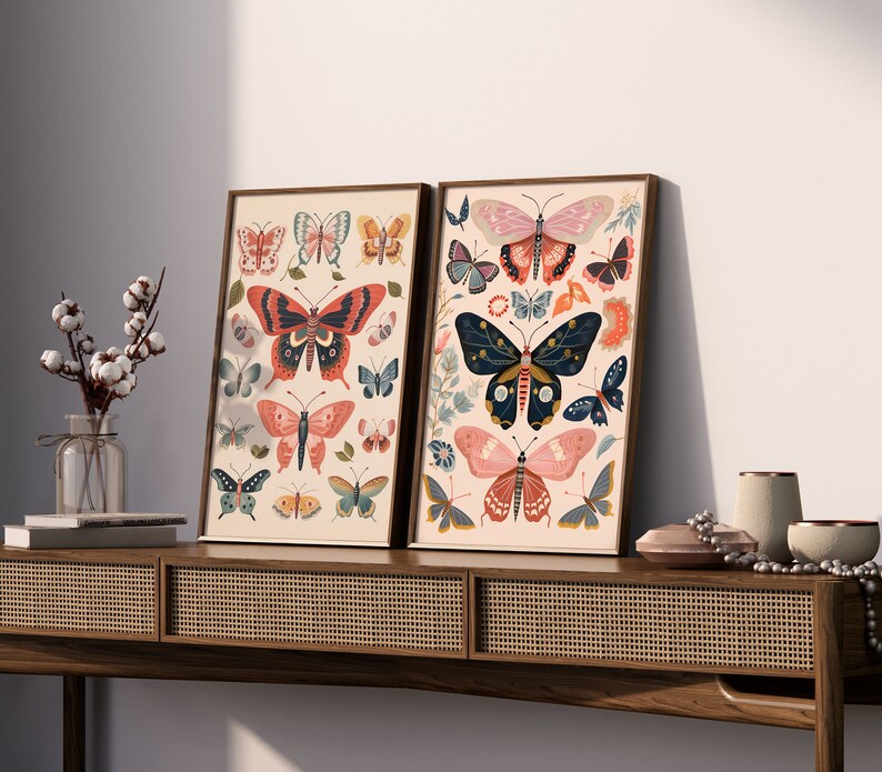 K&ouml;nnte beinhalten: Zwei gerahmte Drucke mit wei&szlig;em Hintergrund und bunten Schmetterlings-Illustrationen. Die Drucke h&auml;ngen an einem Wandregal aus Holz mit einer geflochtenen Rattan-Front.