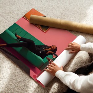 May include: A rolled-up poster and a print featuring a person reclining on a green sofa, with a pink and orange background. The person is wearing a black suit and is holding a glass of wine. The poster is being unrolled.