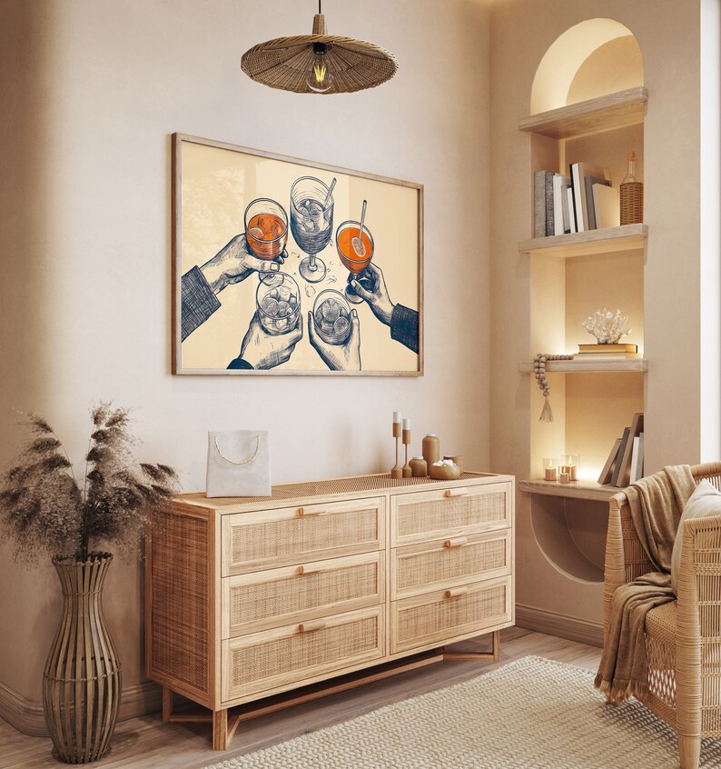 Puede incluir: Una ilustraci&oacute;n enmarcada de cuatro manos sosteniendo vasos de bebidas, con un fondo beige claro. La ilustraci&oacute;n est&aacute; colgada en una pared sobre una c&oacute;moda de madera clara con seis cajones.