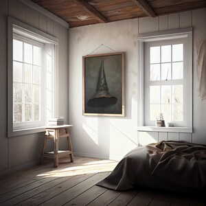 Op de afbeelding: Een slaapkamer met een houten vloer, witte muren en twee ramen. Een bed met een bruin dekbed staat op de voorgrond. Een ingelijst schilderij van een zwarte heksenhoed hangt aan de muur. Een kleine houten kruk met boeken erop staat in de hoek van de kamer.