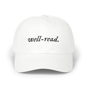 May include: A white baseball cap with a curved peak. The cap has the text "well-read" embroidered in black cursive across the front. The cap has a rounded crown and a button on top.