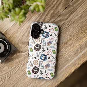 May include: White phone case with a repeating pattern of hockey-themed graphics. The design includes hockey jerseys, skates, hearts, hockey sticks, and the numbers 24 and 81. The case is on a wooden surface.