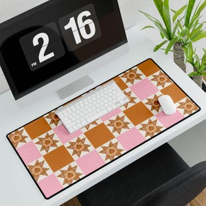 Può includere: Un tappetino da scrivania rettangolare con un motivo patchwork ripetuto composto da quadrati arancioni a tinta unita, quadrati a quadretti rosa chiaro e blocchi a forma di stella bianca. Ogni stella contiene una piccola illustrazione di zucca.