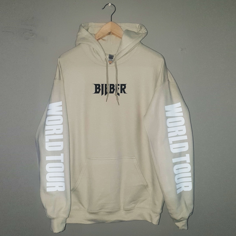 May include: A beige hoodie with the word "BIEBER" printed in black on the front and "WORLD TOUR" printed in white on both sleeves.