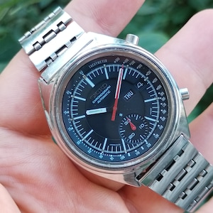 May include: A silver Seiko chronograph wristwatch with a black face and red accents. The watch has a tachymeter scale and a date window that displays "THU".