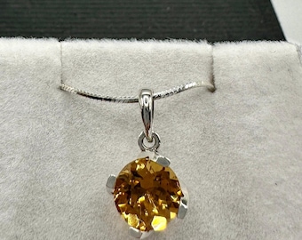 Puede incluir: Un collar de cadena de plata con un colgante que presenta una piedra preciosa redonda y facetada de color topacio.