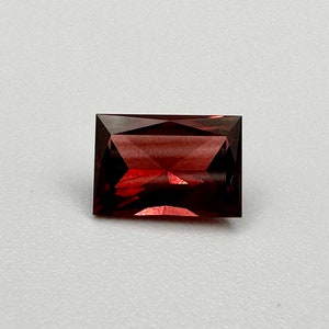 May include: A deep red rectangular gemstone with a faceted cut.