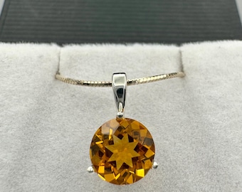 Puede incluir: Un collar con un colgante de oro y una piedra preciosa redonda, facetada y naranja. La piedra preciosa tiene un patrón en forma de estrella en su interior.