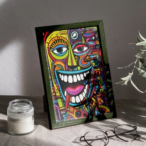 Puede incluir: Una impresión enmarcada de un diseño abstracto colorido con una gran sonrisa de dientes en un esquema de colores verde, amarillo y azul. El marco es de madera verde oscuro.