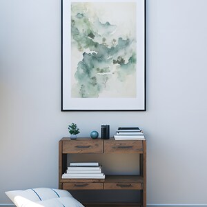 May include: A framed watercolor painting of a misty mountain landscape in shades of green and white, hanging on a white wall above a wooden shelf with books and decorative objects.