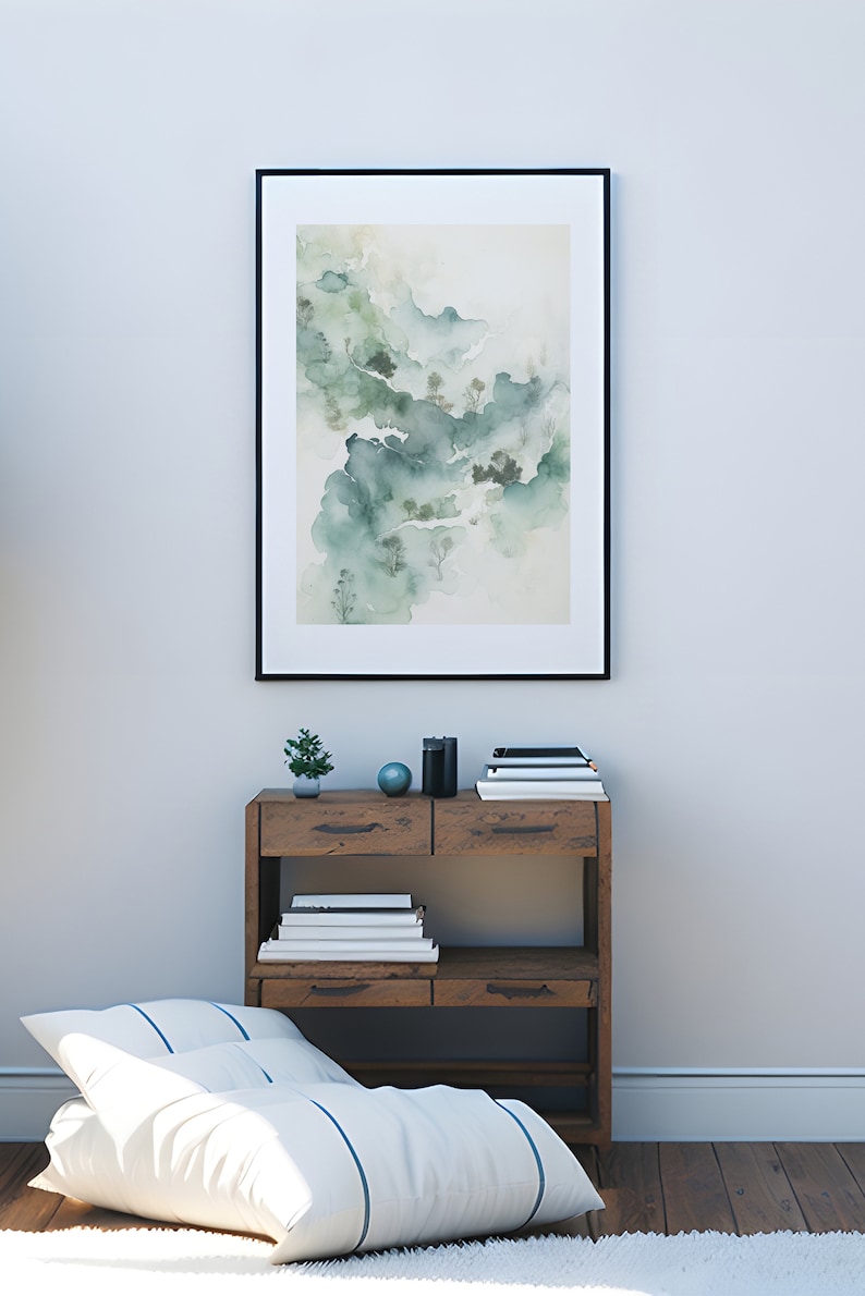 May include: A framed watercolor painting of a misty mountain landscape in shades of green and white, hanging on a white wall above a wooden shelf with books and decorative objects.