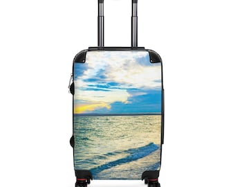 May include: A rolling suitcase featuring a scenic ocean view with a sunset. The image on the suitcase shows a blue ocean, a yellow and orange sunset, and a cloudy sky. The suitcase has a black handle and wheels.