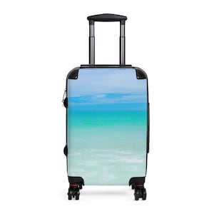 May include: A rolling suitcase featuring a vibrant ocean scene with a blue sky and turquoise water. The luggage has a black handle and frame, with red accents on the wheels. The suitcase is designed for travel.