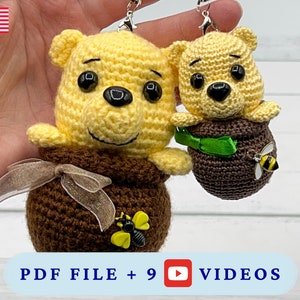Puede incluir: Dos llaveros de Winnie the Pooh tejidos a crochet, uno más grande y otro más pequeño, ambos con cuerpos de tarro de miel marrón y cabezas de oso amarillo. El oso más grande tiene una cinta marrón alrededor del cuello y un amuleto de abeja en su tarro. El oso más pequeño tiene una cinta verde alrededor del cuello y un amuleto de abeja en su tarro.  PDF FILE + 9 VIDEOS