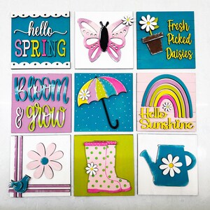 May include: Nine wooden signs with a spring theme. The signs feature a butterfly, an umbrella, a rainbow, a watering can, rain boots, a daisy, and text that says "hello spring", "bloom & grow", "fresh picked daisies", "hello sunshine".