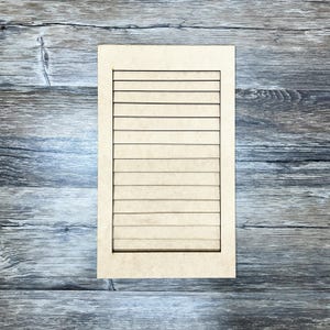 May include: A rectangular wooden sign with horizontal lines, resembling a window shutter. The sign is light brown and set against a weathered, gray wooden background. The lines are evenly spaced and create a textured appearance.