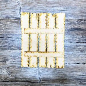 May include: A wooden slatted panel with a distressed, rustic look. The panel has a rectangular shape and is made of thin, light brown wood slats. The slats are arranged in a vertical pattern and are slightly uneven in length. The panel has a rough, unfinished texture and appears to be weathered.