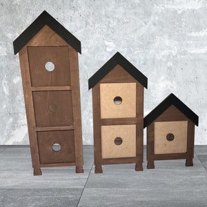 May include: Three wooden storage boxes with black roofs. The boxes are stacked in descending size order. The largest box has three drawers, the middle box has two drawers, and the smallest box has one drawer.