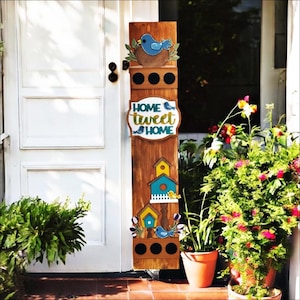 May include: A wooden birdhouse sign with the text "HOME tweet HOME". The sign features a blue bird in a nest, birdhouses, and decorative elements. The sign is brown with blue, yellow, and white accents.