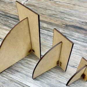 May include: Three wooden picture frames of different sizes, each with a curved base. The frames are made of light brown wood and have a natural finish.