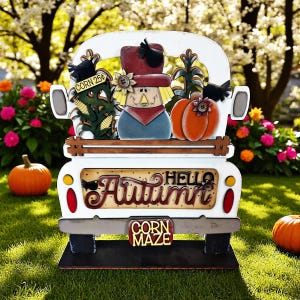 May include: A wooden autumn-themed truck decoration. The truck bed features a scarecrow, pumpkins, and corn stalks. The words "Hello Autumn" are displayed on the truck's side, with "Corn Maze" on the bumper. The truck is white with brown and black accents.