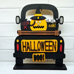 May include: Black wooden truck with a yellow pumpkin, witch hat, and "Halloween Boo!" sign. The truck has red accents and the words "Poison" and "eek!" on the sides.