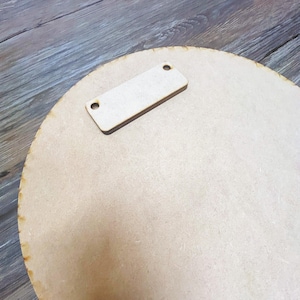 May include: A round, unfinished wooden sign with a rectangular wooden hanger attached to the back.