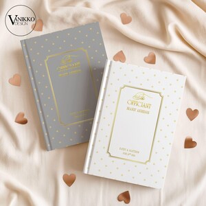Op de afbeelding: Twee hardcover gastenboeken voor bruiloften. Eén is grijs met gouden accenten en de andere is wit met gouden accenten. Beide boeken hebben een goudkleurig omlijnd ontwerp met tekst. Koperkleurige hartvormige confetti is verspreid.