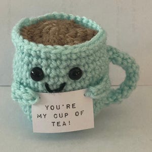 May include: A crocheted teacup with a smiling face and the text "You're my cup of tea!" on a white card.