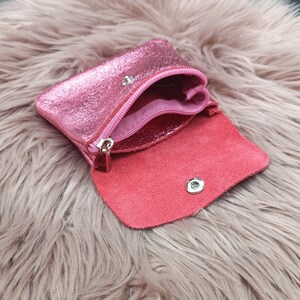 May include: A small, open pink leather coin purse with a metallic sheen. The purse has a zipper closure and a snap closure. The interior is a darker shade of pink. The purse is open, revealing the inside.