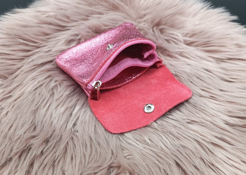 May include: A small, open pink leather coin purse with a metallic sheen. The purse has a zipper closure and a snap closure. The interior is a darker shade of pink. The purse is open, revealing the inside.