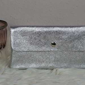 Può includere: Una pochette argentata metallica con una chiusura a scatto.