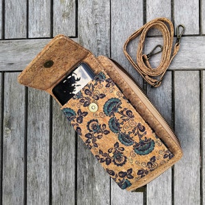 Pode incluir: Uma carteira de corti&ccedil;a com um padr&atilde;o floral em tons de azul, preto e marrom. A carteira tem um fecho de correr e uma al&ccedil;a. Um smartphone preto est&aacute; dentro da carteira.