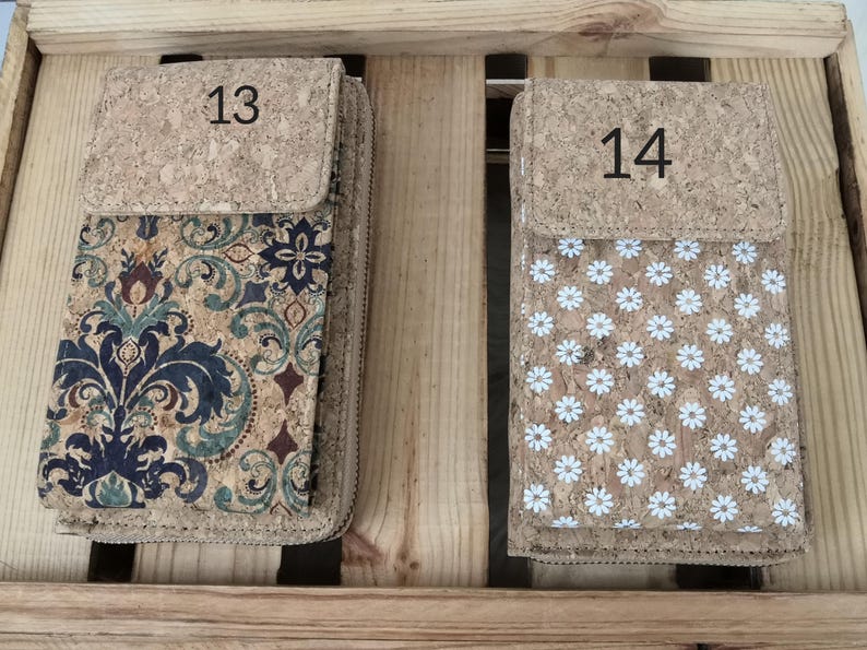 Pode incluir: Duas carteiras de corti&ccedil;a com padr&otilde;es diferentes. A carteira &agrave; esquerda tem um padr&atilde;o floral em tons de azul, verde e marrom. A carteira &agrave; direita tem um padr&atilde;o de margarida branca em um fundo de corti&ccedil;a. A carteira &agrave; esquerda tem o n&uacute;mero 13 na frente e a carteira &agrave; direita tem o n&uacute;mero 14 na frente.