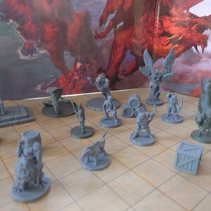 May include: A collection of grey plastic miniature figurines, including a dragon, a tree, a mushroom, a throne, a barrel, a box, and several human and animal figures. The miniatures are arranged on a grey tiled surface.