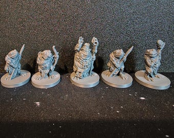 May include: Five gray miniature frog figurines, each on a circular base. The frogs are in various poses, some holding weapons or staffs. The figurines are detailed and appear to be 3D-printed, suitable for tabletop gaming or collecting.