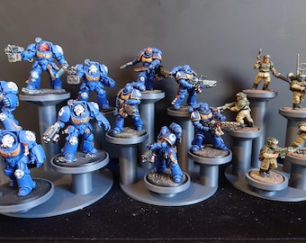 May include: A collection of miniature plastic figurines arranged on tiered gray circular stands. The group includes several blue armored space soldiers with helmets and weapons, alongside smaller soldiers in tan uniforms with green helmets.