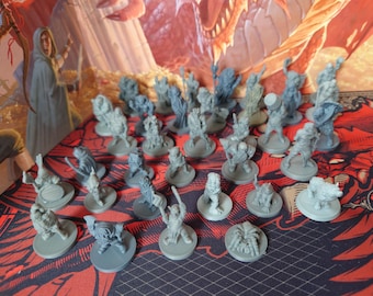 May include: A collection of unpainted gray plastic miniature figurines depicting various fantasy characters and creatures, each mounted on a circular base, arranged in a group on a surface featuring a red and black dragon-themed graphic print.