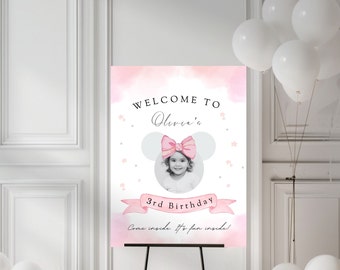 Può includere: Un cartello di benvenuto rosa e bianco con una silhouette di testa di Minnie Mouse. Il cartello dice "Benvenuti al 3° compleanno di Olivia. Entrate, è divertente dentro!"