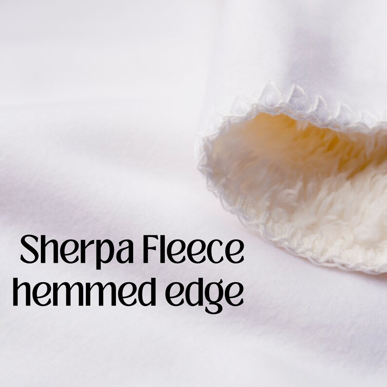May include: Close-up of a white sherpa fleece fabric with a hemmed edge. The fabric is soft and fluffy, and the hemmed edge is neatly finished.