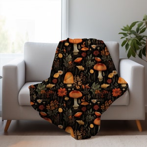 May include: A black throw blanket with a repeating pattern of orange and brown mushrooms and green leaves on a black background.