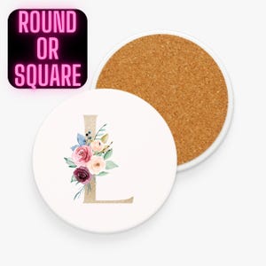 May include: White round coaster with a floral design and the letter "L" in gold. The coaster features a bouquet of pink, burgundy, and peach flowers with green and blue leaves. The text "ROUND OR SQUARE" is in a pink neon font.