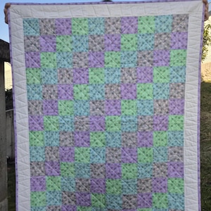 Może przedstawiać: Kołdra patchworkowa z białą obwódką i szachownicowym wzorem z fioletowej, zielonej i niebieskiej tkaniny kwiatowej.